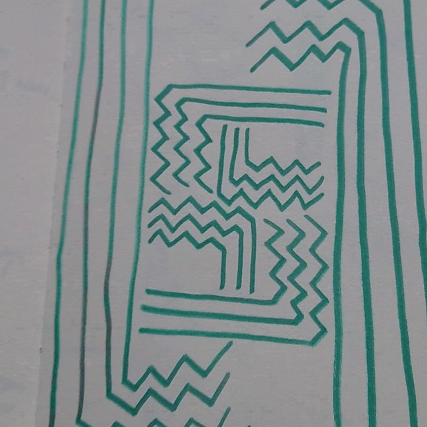 An open notebook or sketchbook lying on a gray textured carpet, featuring green hand-drawn geometric patterns on the pages.